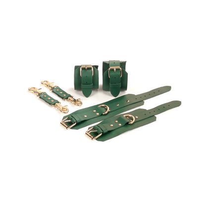 Green leather BDSM set laid flat: wrist cuffs and ankle cuffs with buckle straps, rivets, adjustment holes, and gold-tone hardware. Each cuff includes a 2.5 cm D-ring. Two matching leather connectors with gold-tone carabiners on both ends are placed next to the set.