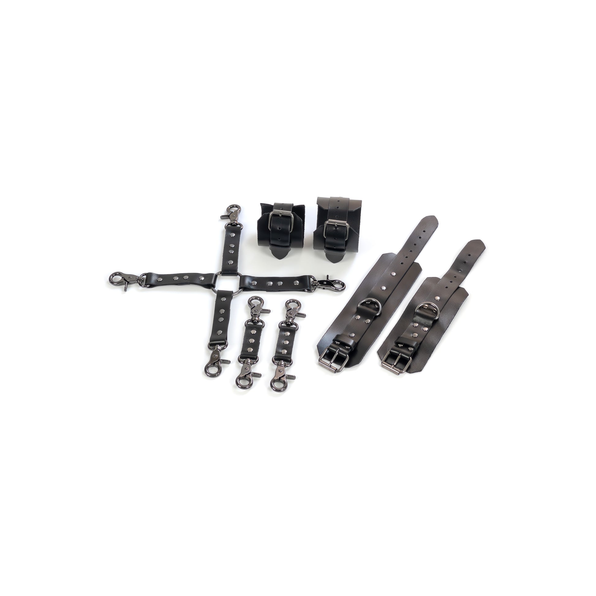 Complete leather restraint set laid out on a white background, black genuine leather with dark nickel hardware, includes handcuffs, ankle cuffs, one four-way connector and two small connectors, cuffs shown opened and fastened to show 2.5 cm straps, buckles and 2.5 cm D-rings.