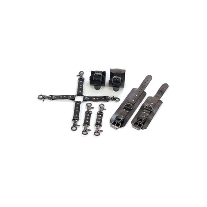 Complete leather restraint set laid out on a white background, black genuine leather with dark nickel hardware, includes handcuffs, ankle cuffs, one four-way connector and two small connectors, cuffs shown opened and fastened to show 2.5 cm straps, buckles and 2.5 cm D-rings.