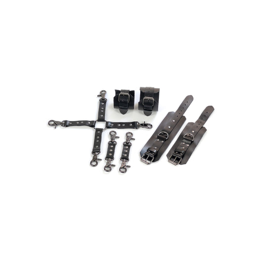 Complete leather restraint set laid out on a white background, black genuine leather with dark nickel hardware, includes handcuffs, ankle cuffs, one four-way connector and two small connectors, cuffs shown opened and fastened to show 2.5 cm straps, buckles and 2.5 cm D-rings.