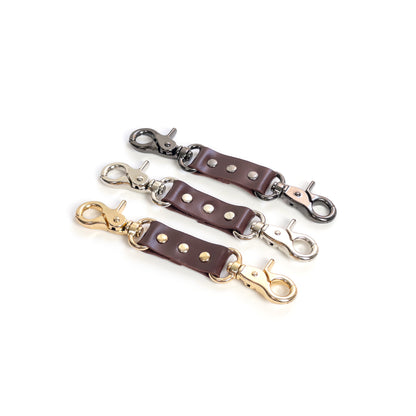 Leather double carabiner connector made of marsala genuine leather with metal carabiners fixed on both ends, photographed on a white background. The image shows marsala leather combined with gold, silver, and dark nickel carabiners, with the connector laid flat to clearly display the strap and both carabiners.