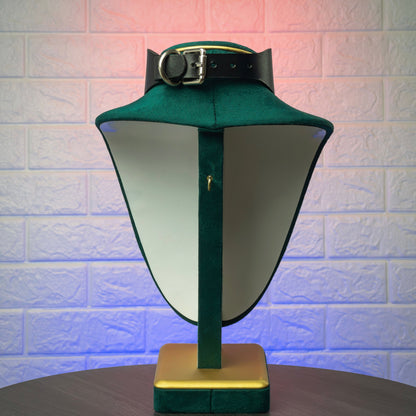 A black choker on a stand against a textured wall.