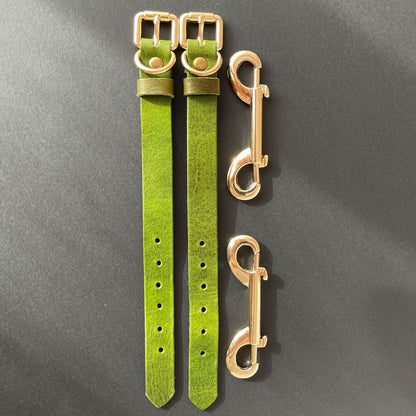 Two green leather cuffs straps with gold buckles on a gray background