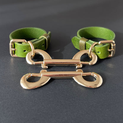 Green leather handcuffs with gold metal clasps on a dark background