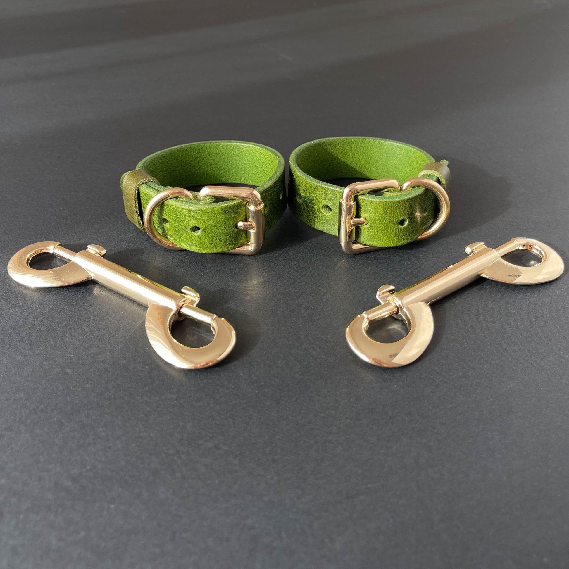 Two green leather handcuffs with brass hardware on a gray background