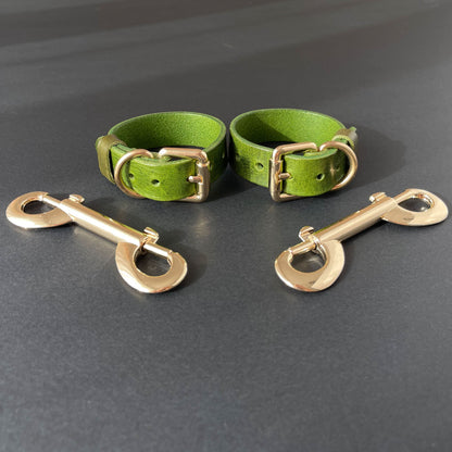 Two green leather handcuffs with brass hardware on a gray background