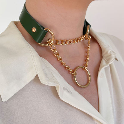 Green leather choker with gold hardware and O-ring, worn over a cream shirt. Decorative layered chains.

