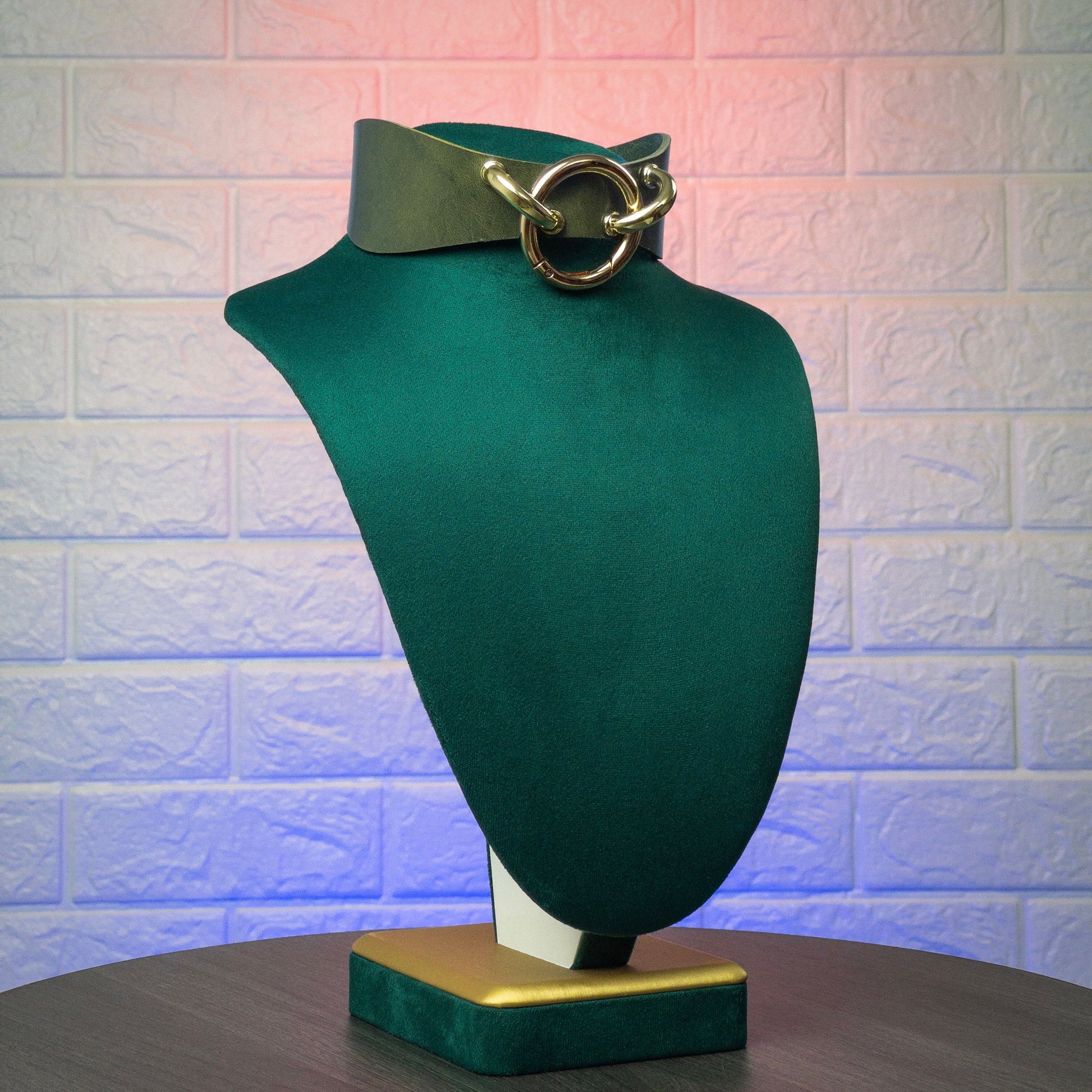Green collar with a gold buckle on a green mannequin bust against a textured white wall.