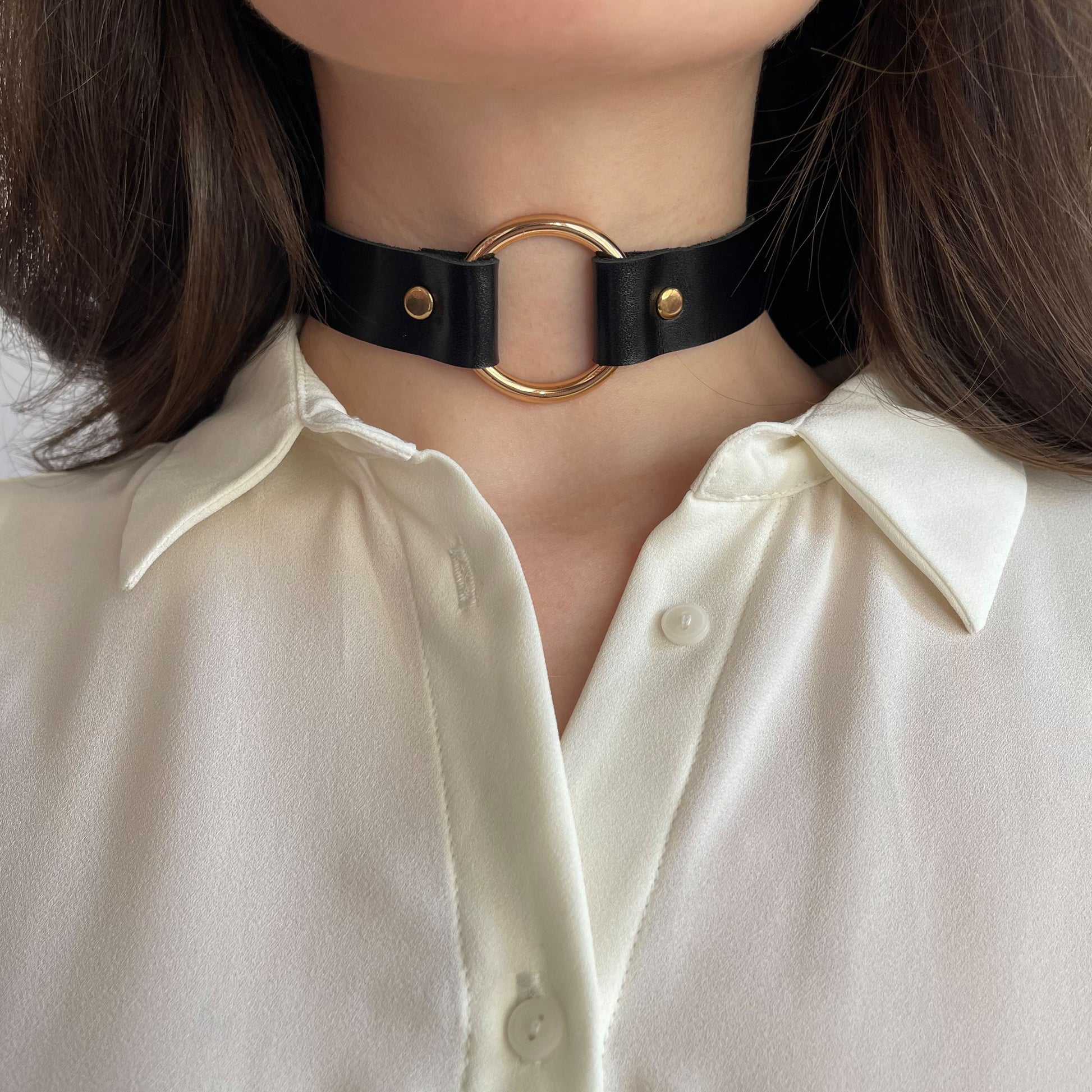 Centered front shot of black leather choker featuring gold O-ring and matching rivets