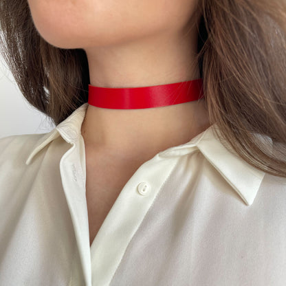 Bold red leather choker made from semi-matte genuine leather (1.4–1.8 mm thick), 1.5 cm (0.59 in) wide, with buckle closure. The vivid color pops against a white shirt, worn by a woman in a close-up. A striking yet wearable accessory, perfect for confident daily looks or bold styling statements.