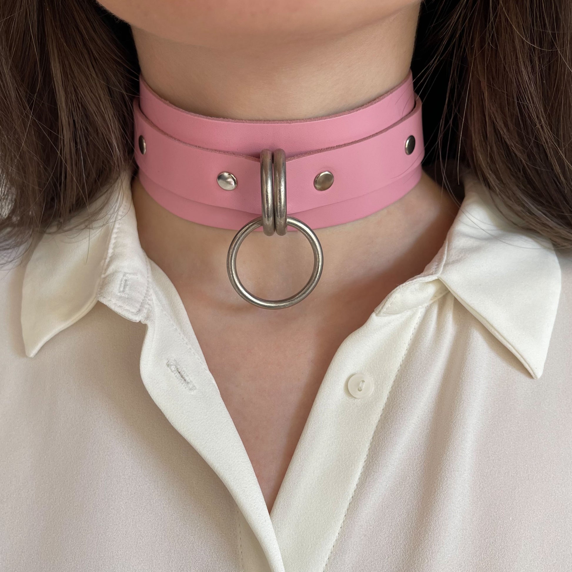 Front view of a pink leather wide choker with silver hardware. The central round O-ring is attached to two D-rings on the wide leather band. The collar sits evenly on the neck, showing the straight cut leather edges and metal hardware clearly.