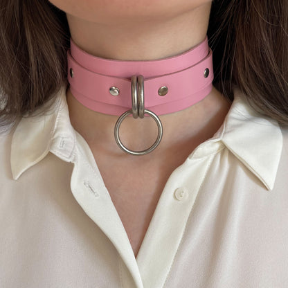 Front view of a pink leather wide choker with silver hardware. The central round O-ring is attached to two D-rings on the wide leather band. The collar sits evenly on the neck, showing the straight cut leather edges and metal hardware clearly.