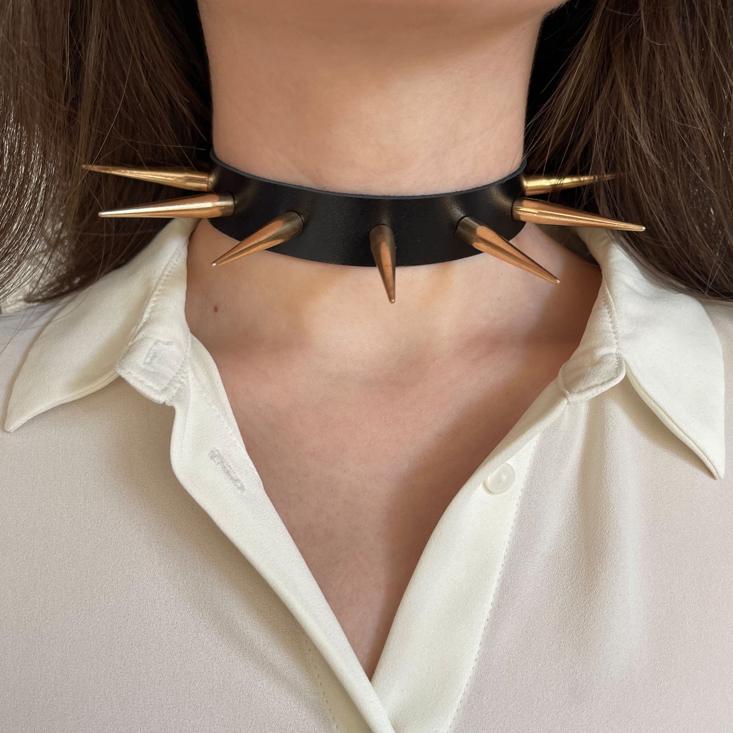 Leather spiked collar worn on the neck, front view, with long gold-colored cone spikes across the collar