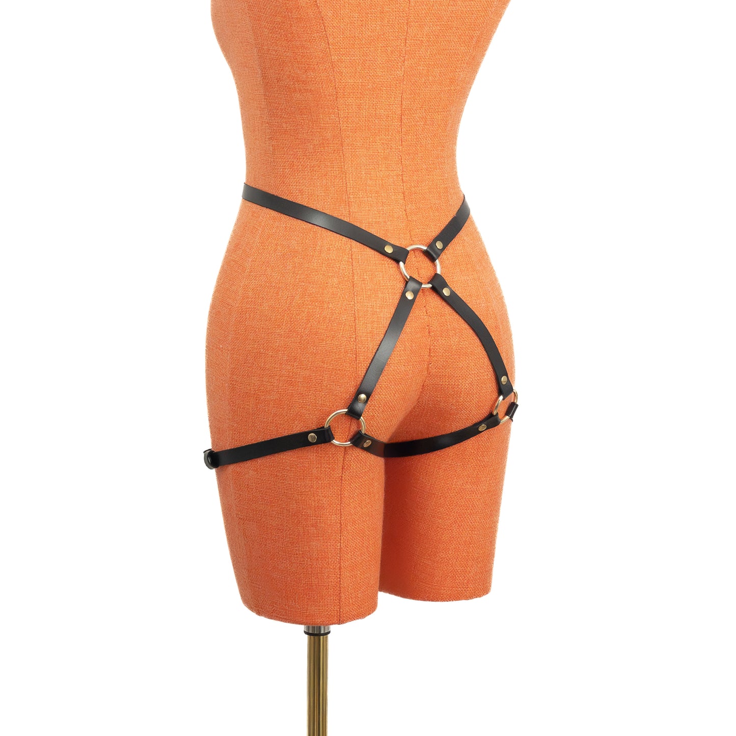 Slim leather butt garter in black leather with gold hardware, angled rear view on mannequin, narrow straps forming a back ring connection and extending toward outer thigh bands.