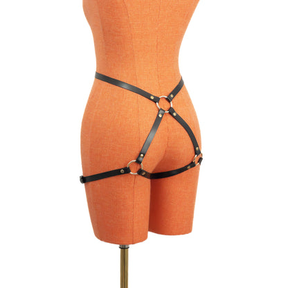 Slim leather butt garter in black leather with gold hardware, angled rear view on mannequin, narrow straps forming a back ring connection and extending toward outer thigh bands.