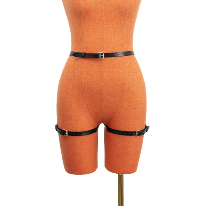 Slim leather butt garter made of black leather with gold hardware, front view on mannequin, slim waist strap and minimal thigh bands visible.