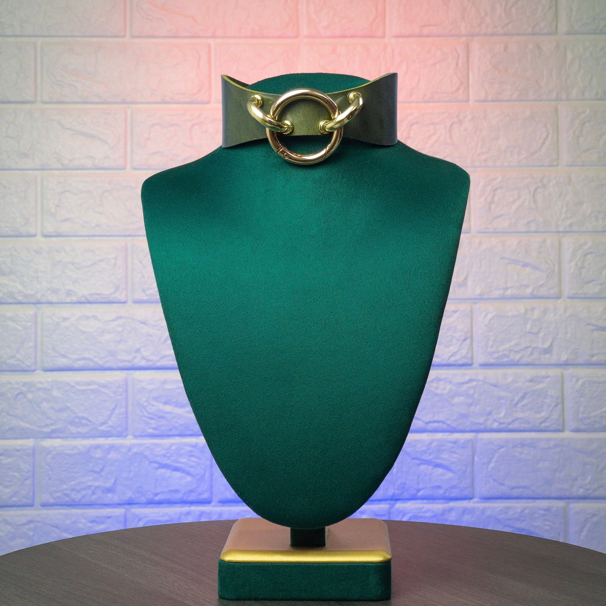 Green mannequin head with a green collar and gold hardware on a textured white background