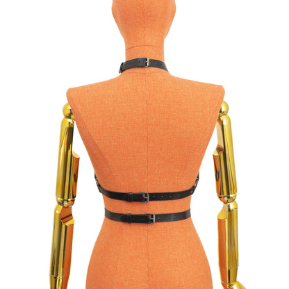 Back view of a black leather open chest harness on a mannequin, showing the buckle closure on the neck strap and two buckle closures on the underbust straps, with straps wrapping around the torso and connecting to the front ring structure; dark nickel hardware; leather thickness 1.4–1.8 mm.