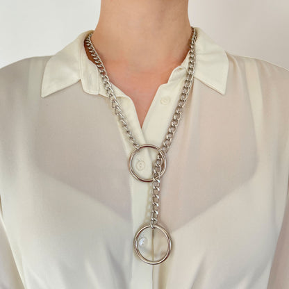 Silver-tone sliding chain choking collar worn on the neck over light clothing. One 30 mm (1.18 in) ring sits closer to the neck, while the second ring hangs lower. The metal chain passes through the upper ring, clearly showing the sliding tightening mechanism.