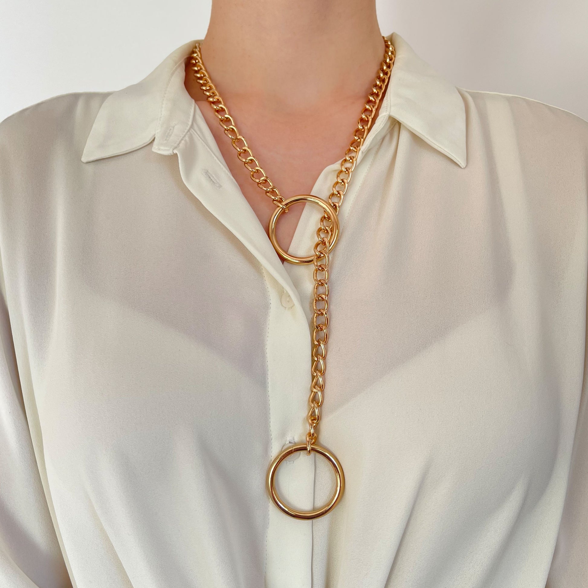 Gold-tone sliding chain choking collar worn on the neck. The warm metal chain contrasts with the fabric underneath. A 30 mm (1.18 in) round ring is positioned near the neck, while the second ring hangs freely, showing how pulling it would tighten the collar.