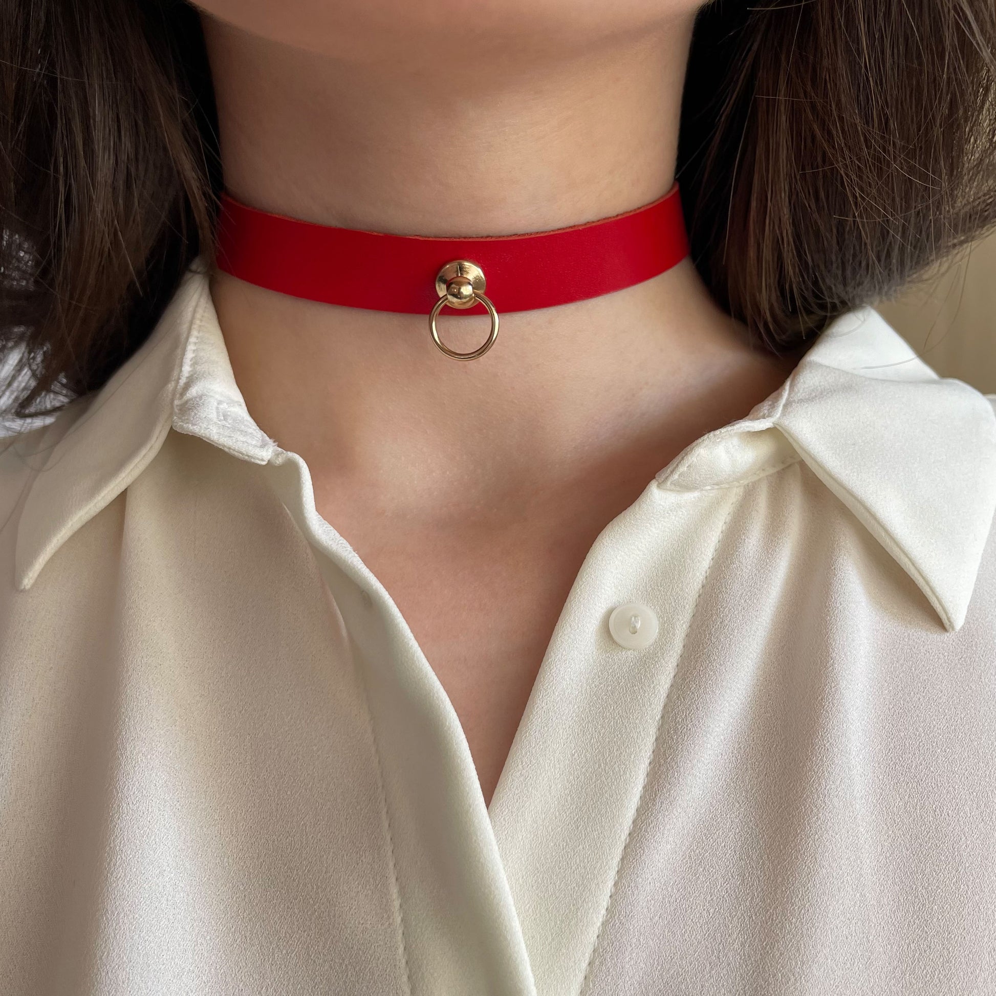 Bold red leather choker with a central golden ring. Crafted from genuine semi-matte leather, 1.5 cm (0.59 in) wide. Shown front-facing on a woman in a white blouse, the piece offers a confident visual accent for everyday or daring looks.