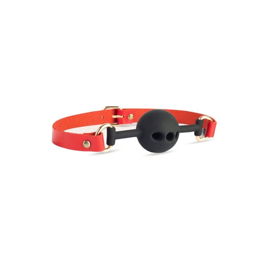 Leather ball gag in genuine red leather with gold metal hardware and black silicone ball. Angled side view on white background shows riveted strap attachment to metal D-rings and buckle closure. Strap width 5/8 inch (1.5 cm), leather thickness 3–4 oz (1.4–1.8 mm).