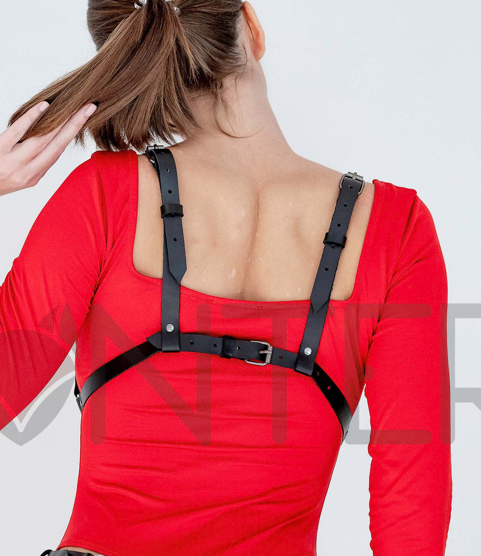 Open Cup Leather Bra worn on model, back view, genuine black leather with silver hardware, one horizontal back strap and two vertical adjustable shoulder straps with buckles, classic bra-style closure visible; strap width 5/8 inch (15 mm), leather thickness 3–4 oz (1.4–1.8 mm).