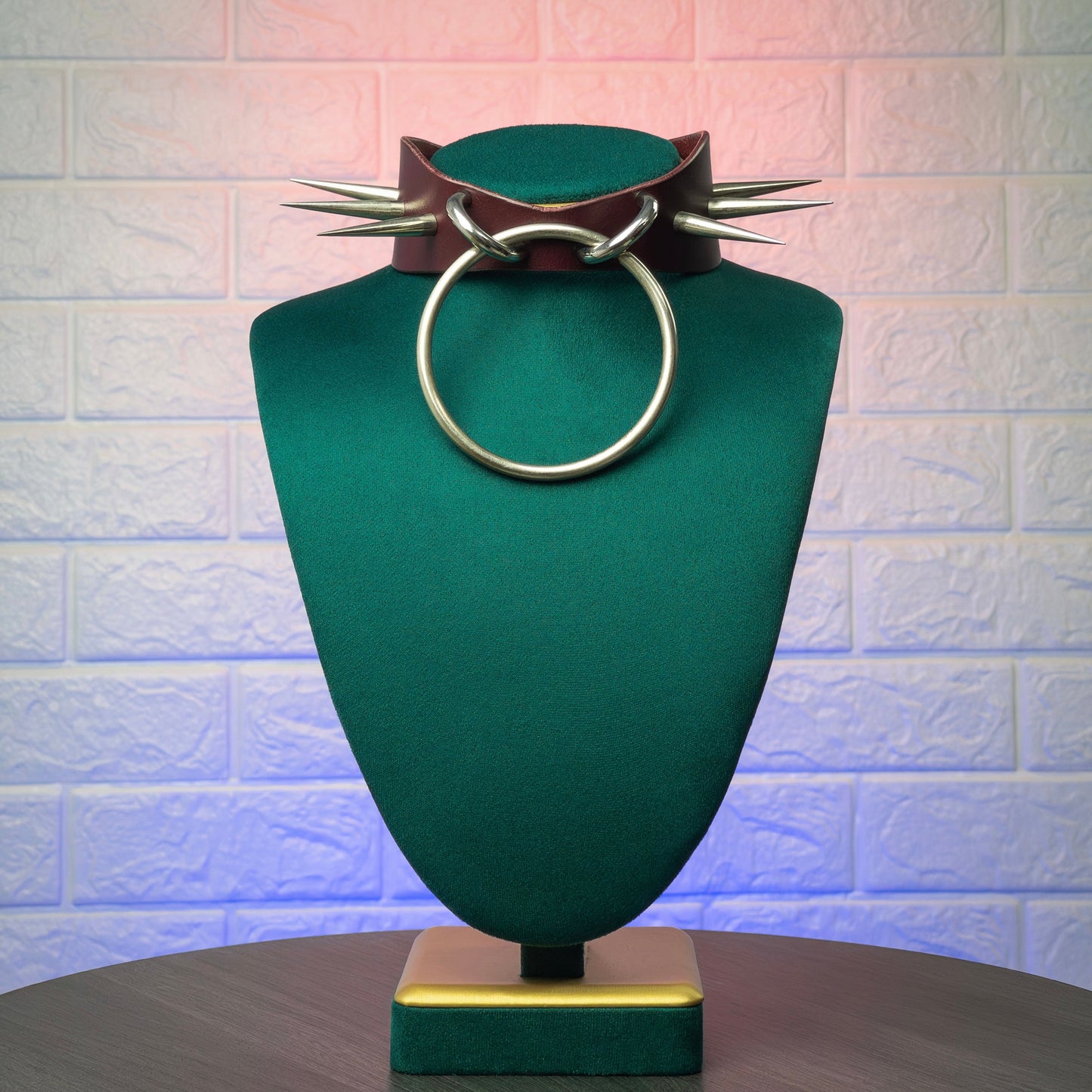 Jewelry display with a marsala leather collar and circular metal ring and spikes on a textured background