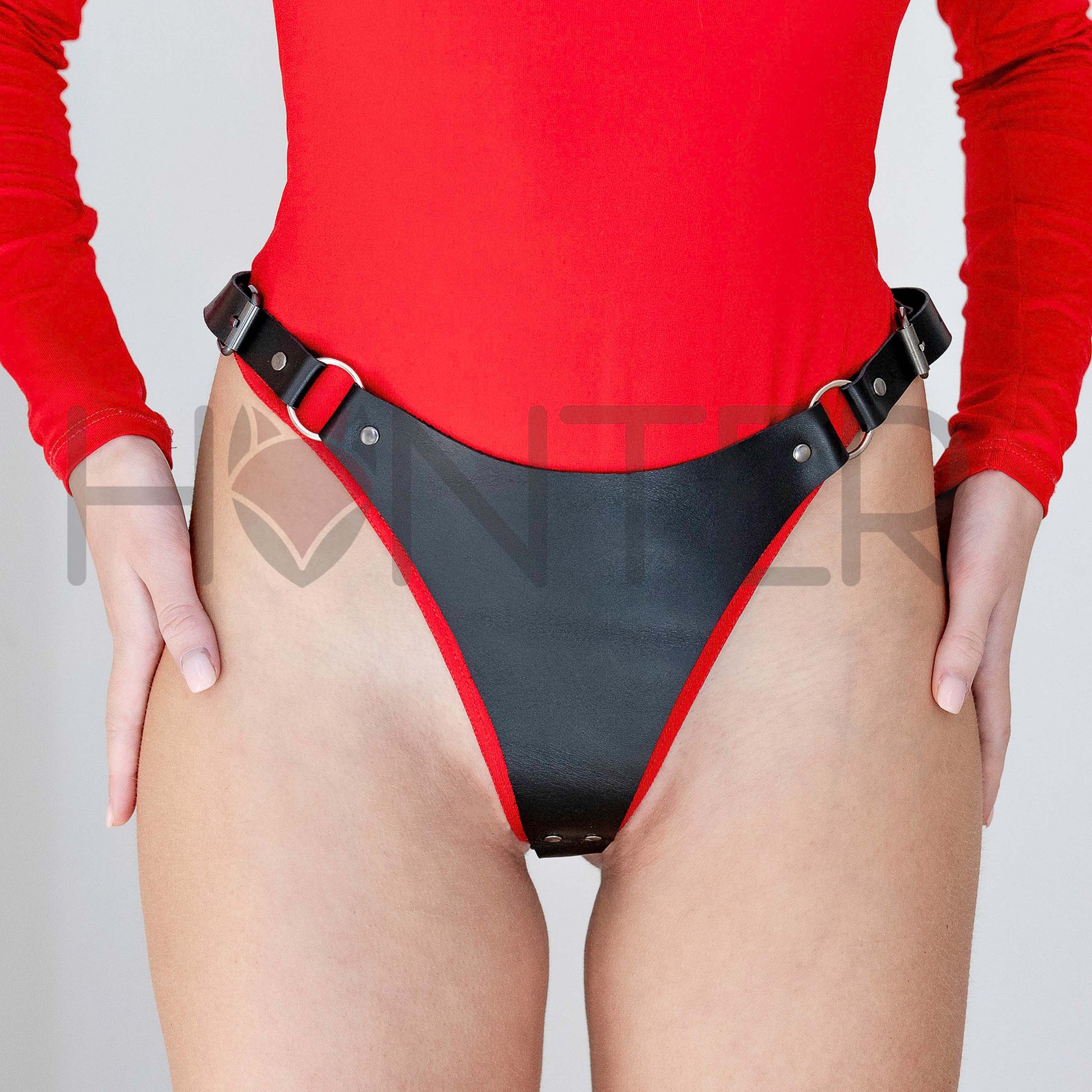 Front view of a model wearing black leather thong with metal rings and side buckle straps. The structured front panel connects to adjustable hip straps through rings, showing independent side buckle fastening.
