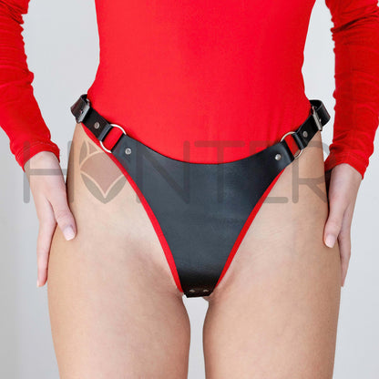 Front view of a model wearing black leather thong with metal rings and side buckle straps. The structured front panel connects to adjustable hip straps through rings, showing independent side buckle fastening.