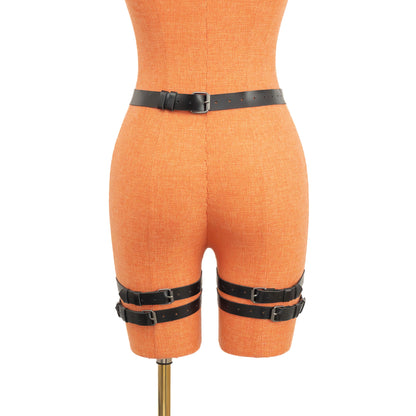 Rear view of the black leather garter belt on a mannequin. The 1 inch (2.5 cm) waist strap fastens with a dark nickel buckle, and two vertical straps descend to double 3/4 inch (2 cm) thigh bands secured with matching metal buckles on the back of each leg.