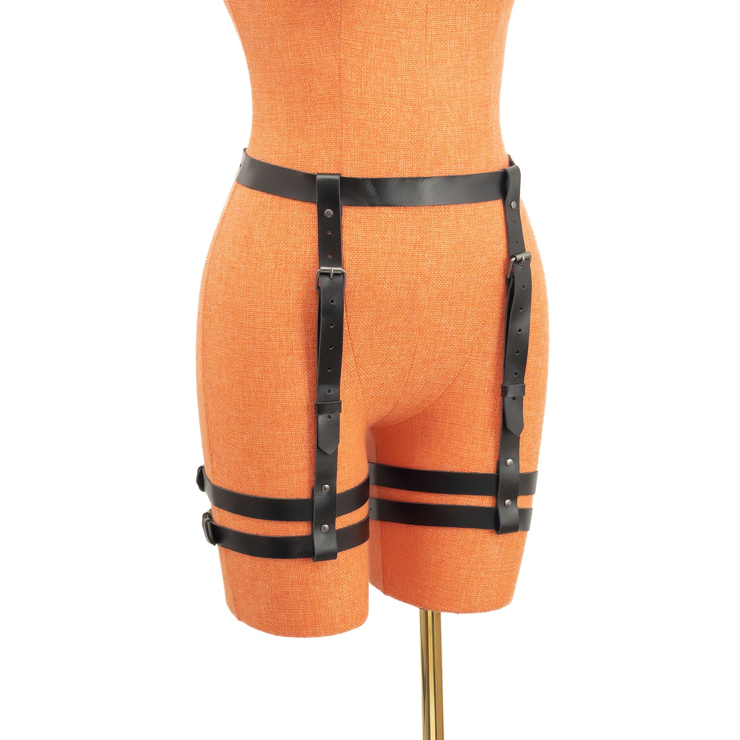 Semi-side view of the leather garter belt displayed on a mannequin. The 1 inch (2.5 cm) waist strap and vertical 3/4 inch (2 cm) straps form a structured line toward the double thigh bands, with dark nickel buckles and adjustment holes visible along the straps.