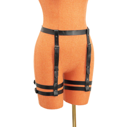 Semi-side view of the leather garter belt displayed on a mannequin. The 1 inch (2.5 cm) waist strap and vertical 3/4 inch (2 cm) straps form a structured line toward the double thigh bands, with dark nickel buckles and adjustment holes visible along the straps.
