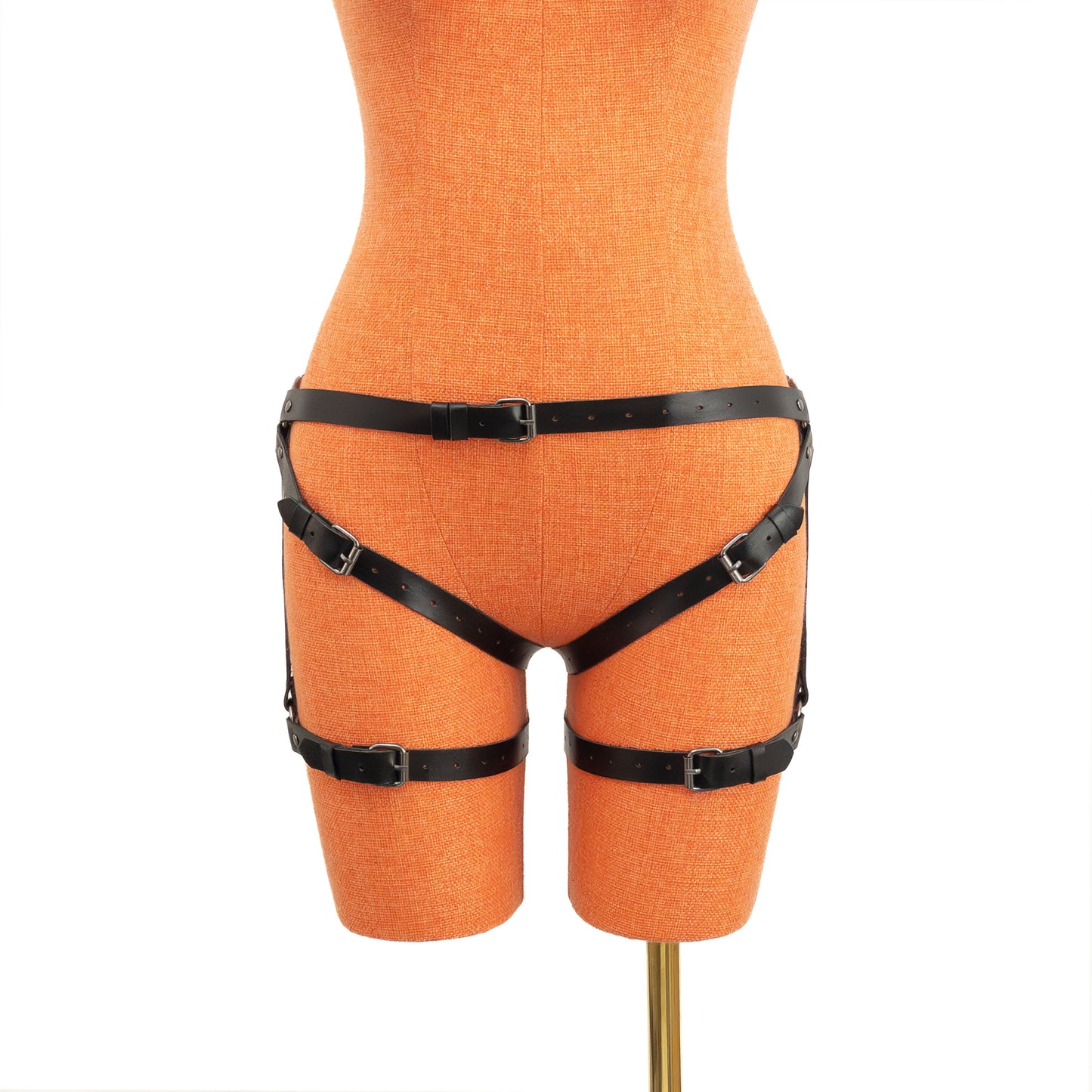 Leather thigh strap harness in black genuine leather with dark nickel hardware, front view on mannequin, waist belt secured with buckle, vertical strap connecting to thigh ring and lower thigh band.