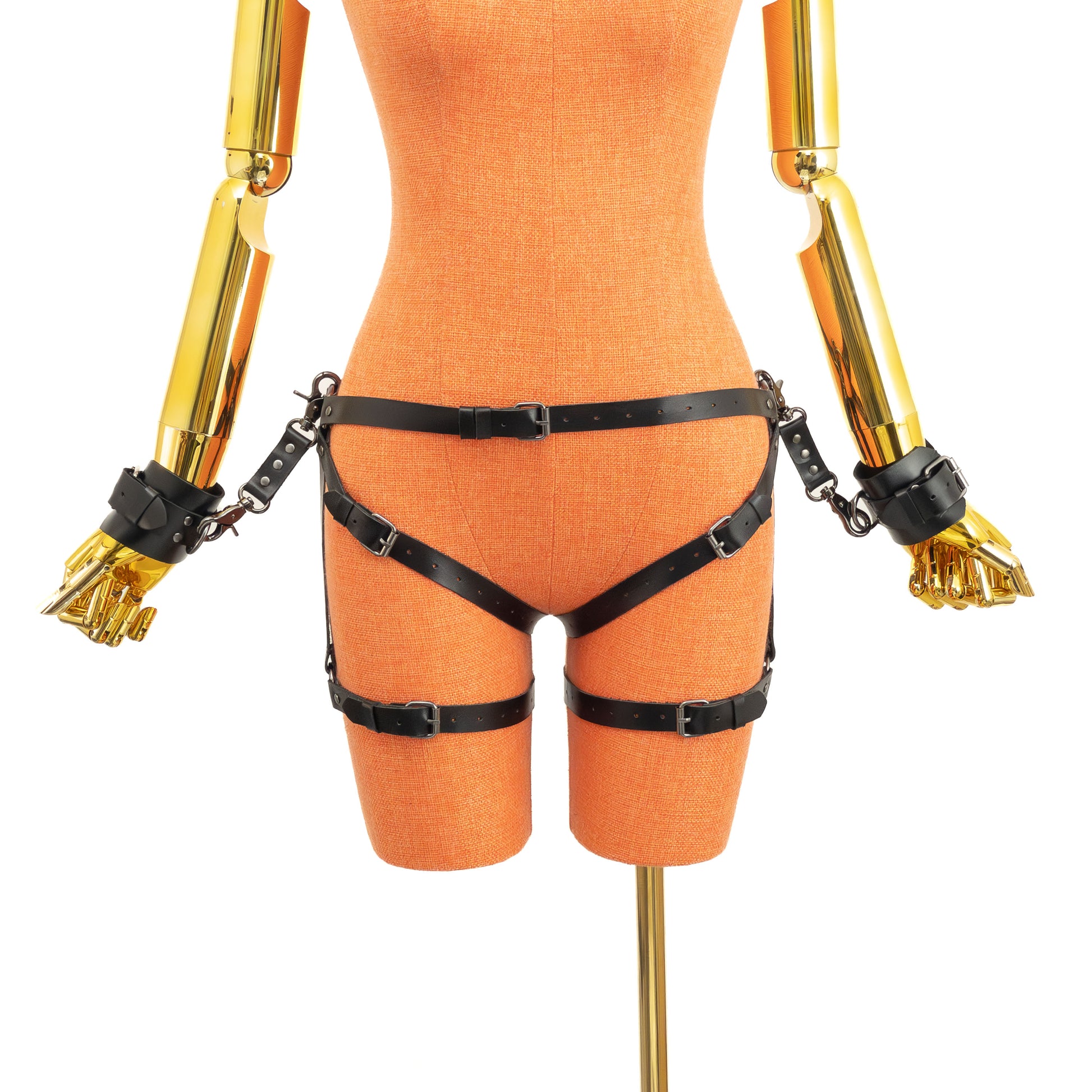 Front view of an open crotch hip ring garter belt set on a mannequin in black leather, showing the waist strap with front buckle, side hip rings, straps passing through the crotch, lower leg rings, adjustable thigh straps, and wrist cuffs attached to the side rings by leather connectors with carabiners.