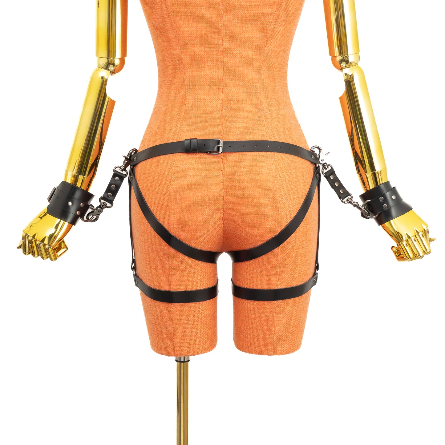 Back view of an open crotch hip ring garter belt set on a mannequin in black leather, showing the back waist buckle, side hip rings, straps running under the buttocks and through the crotch, lower leg rings, thigh straps with buckles, and wrist cuffs attached at both sides.