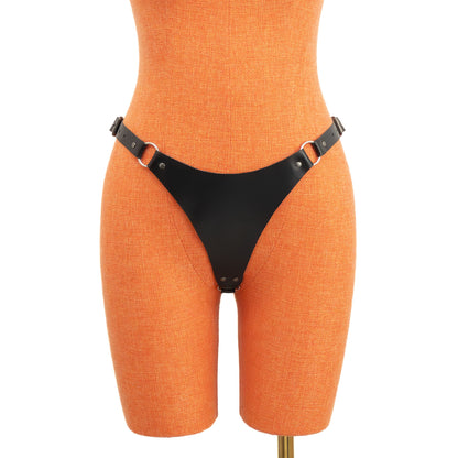 Front view of black leather thong on orange mannequin showing the wide front panel with ring connections and side buckle straps forming a defined structured shape.