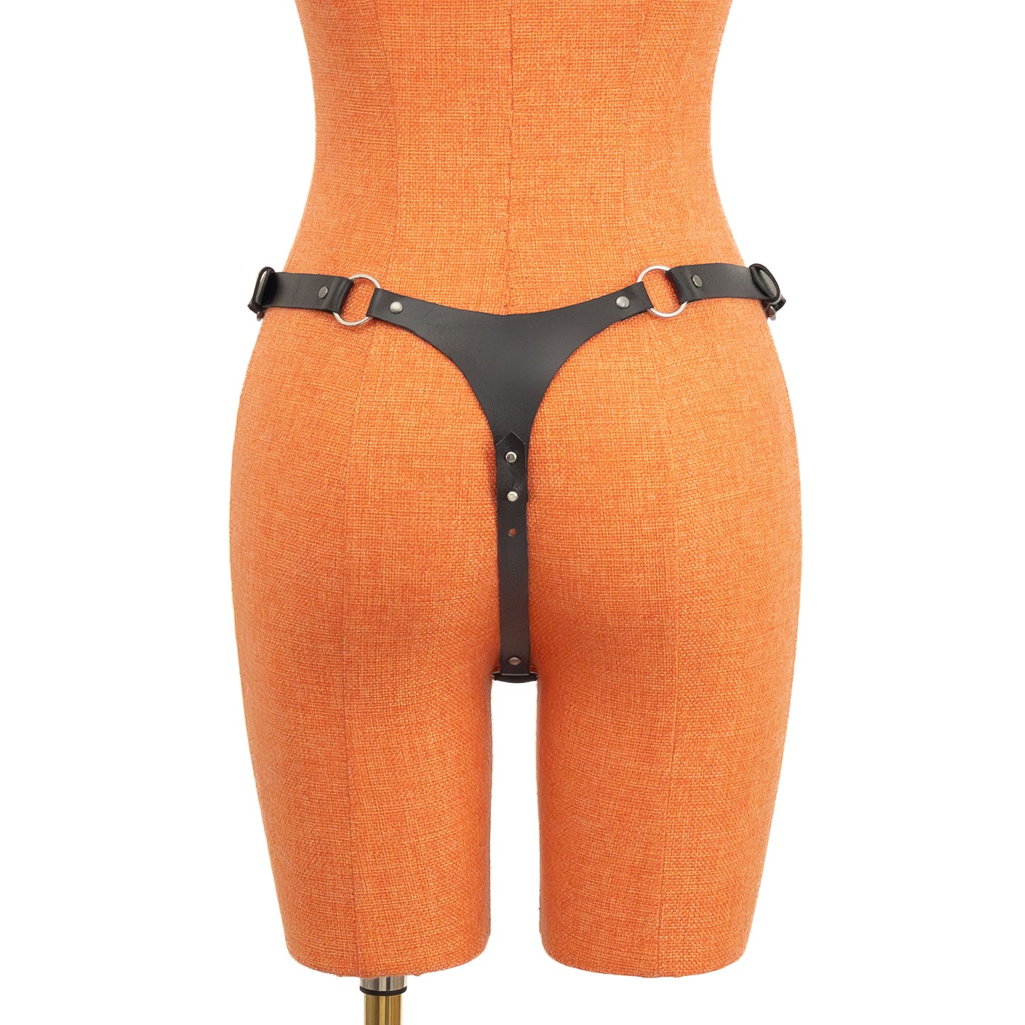 Rear view of black leather thong on orange mannequin. A small triangular back panel connects to side straps through rings, and the center strap runs between the legs with screw-based length adjustment.