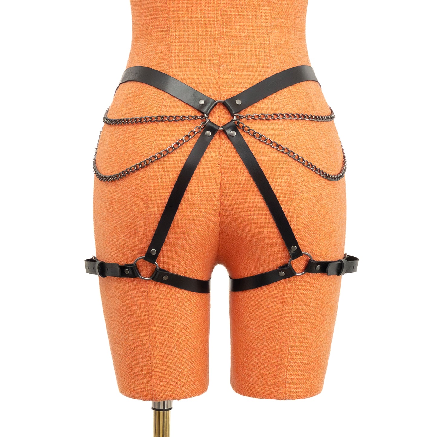 Rear view of the black leather butt garter on an orange mannequin. Chains run from front belt rings toward a central back ring positioned on the butt area, forming a double-chain pattern across the hips and butt. Thigh straps fasten with dark nickel buckles.