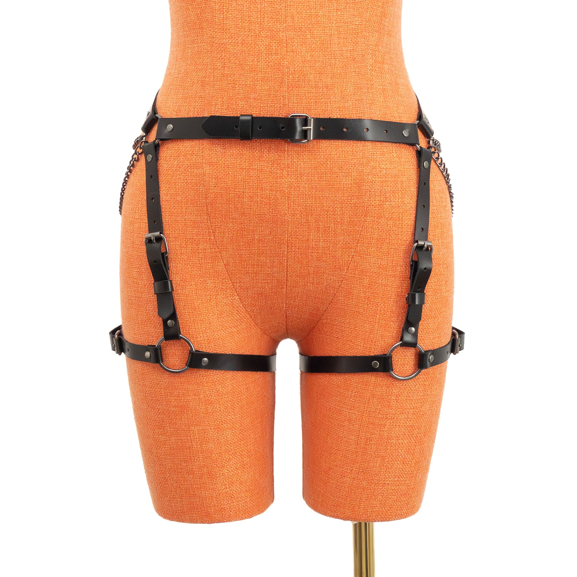Front view of the black genuine leather butt garter displayed on an orange mannequin. A narrow waist strap with a center front buckle connects to vertical adjustable straps and horizontal thigh straps positioned evenly around both legs.