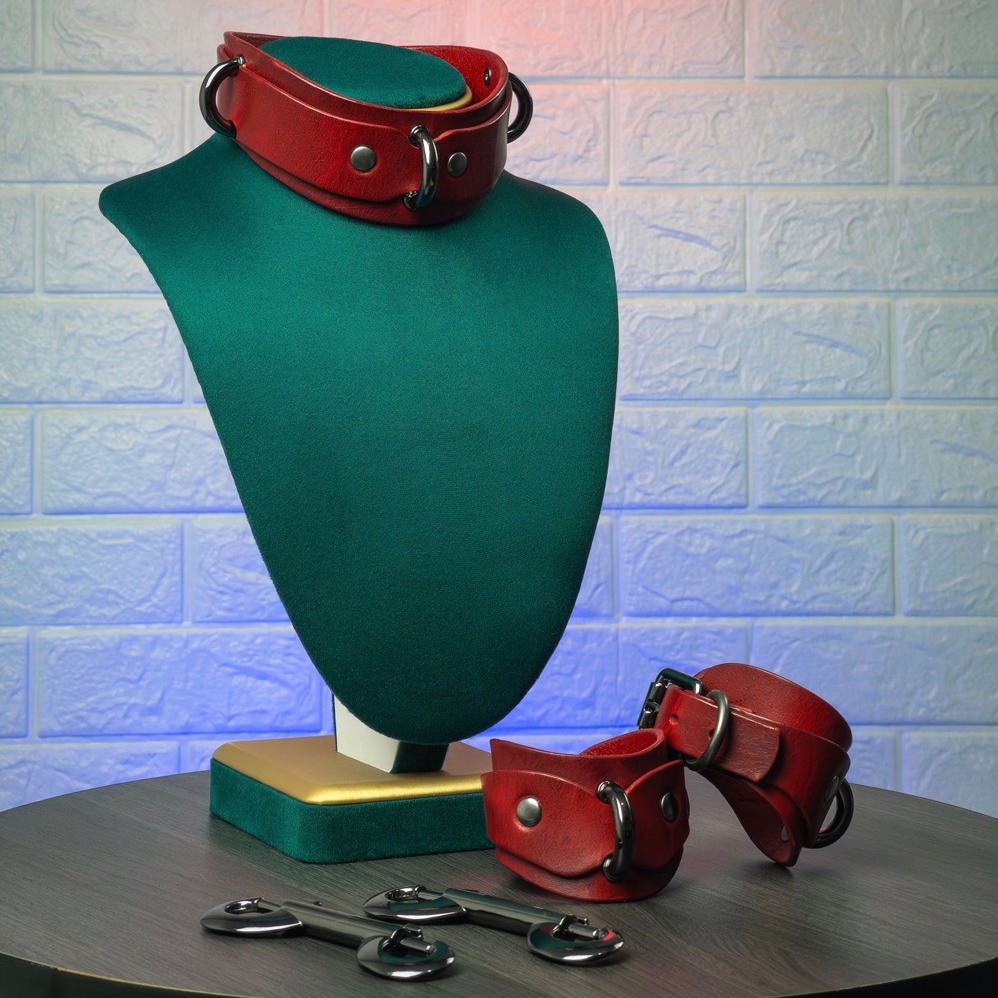 Red leather collar and cuffs on a green mannequin bust against a textured white brick wall.