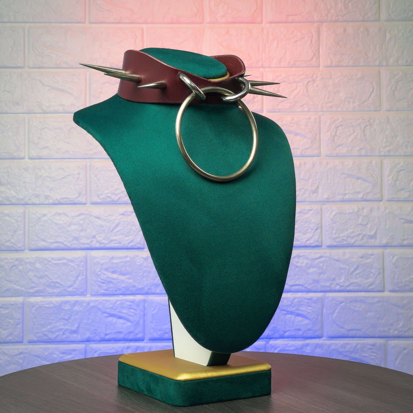 Green mannequin bust with leather collar and metal ring against a textured white wall.