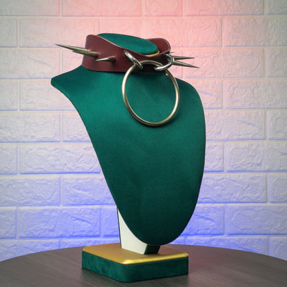 Green mannequin bust with leather collar and metal ring against a textured white wall.