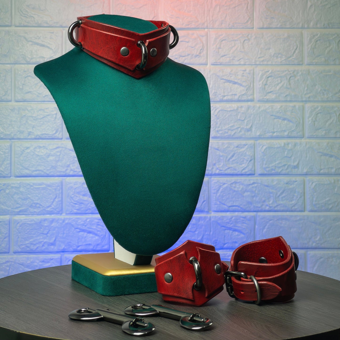 Red leather collar and cuffs on a green mannequin bust against a textured white wall.