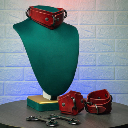 Red leather collar and cuffs on a green mannequin bust against a textured white wall.