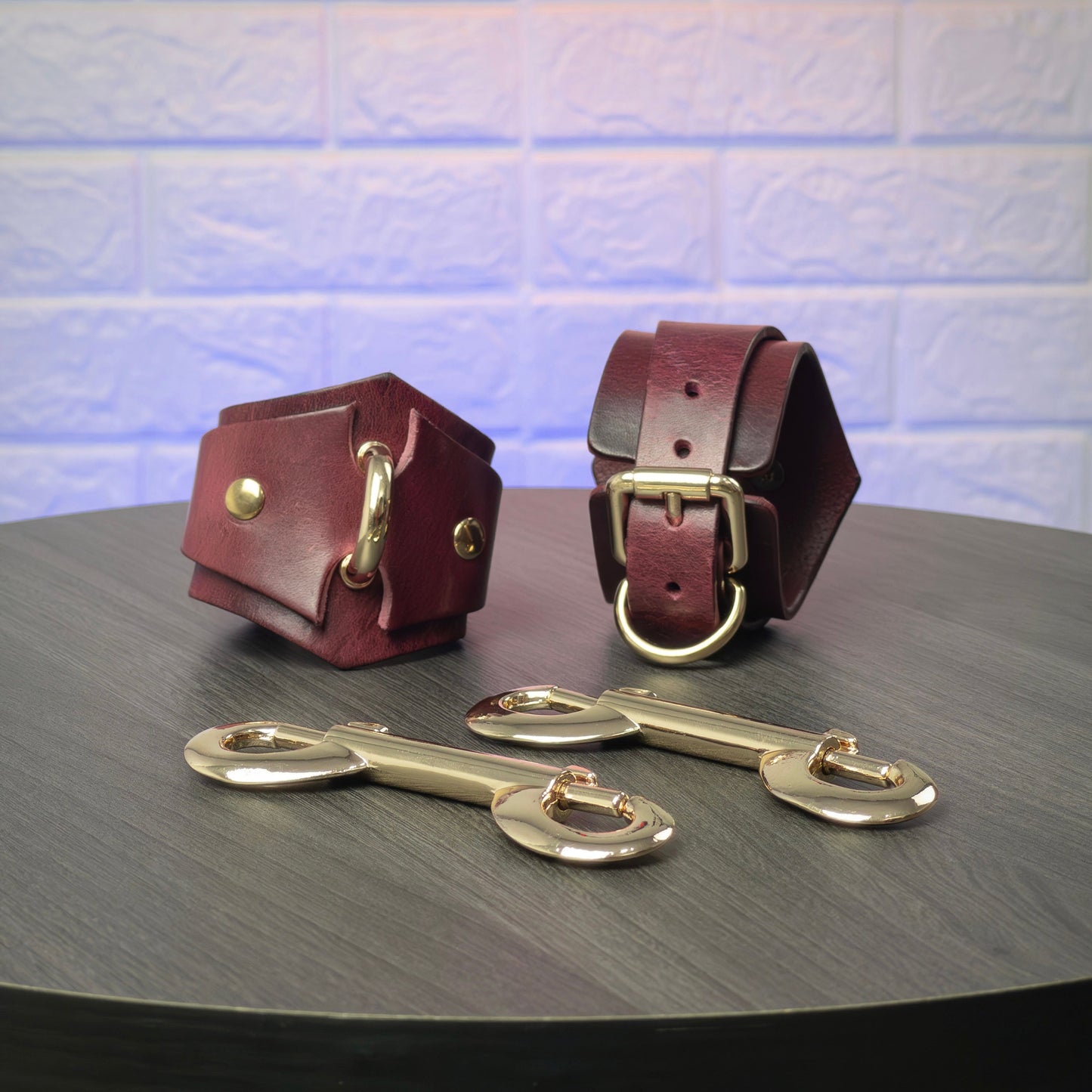Two leather handcuffs with metal buckles on a dark surface.