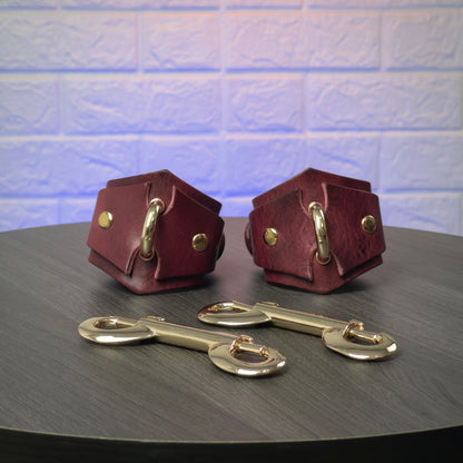 Two leather handcuffs with gold hardware on a dark surface against a textured light blue background.