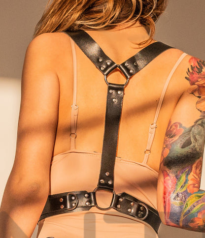 Back view of the harness worn on a model, showing two shoulder straps joining into a single vertical strap connected to a ring between the shoulder blades and continuing to the central ring on the wide waist belt; dark nickel hardware visible.
