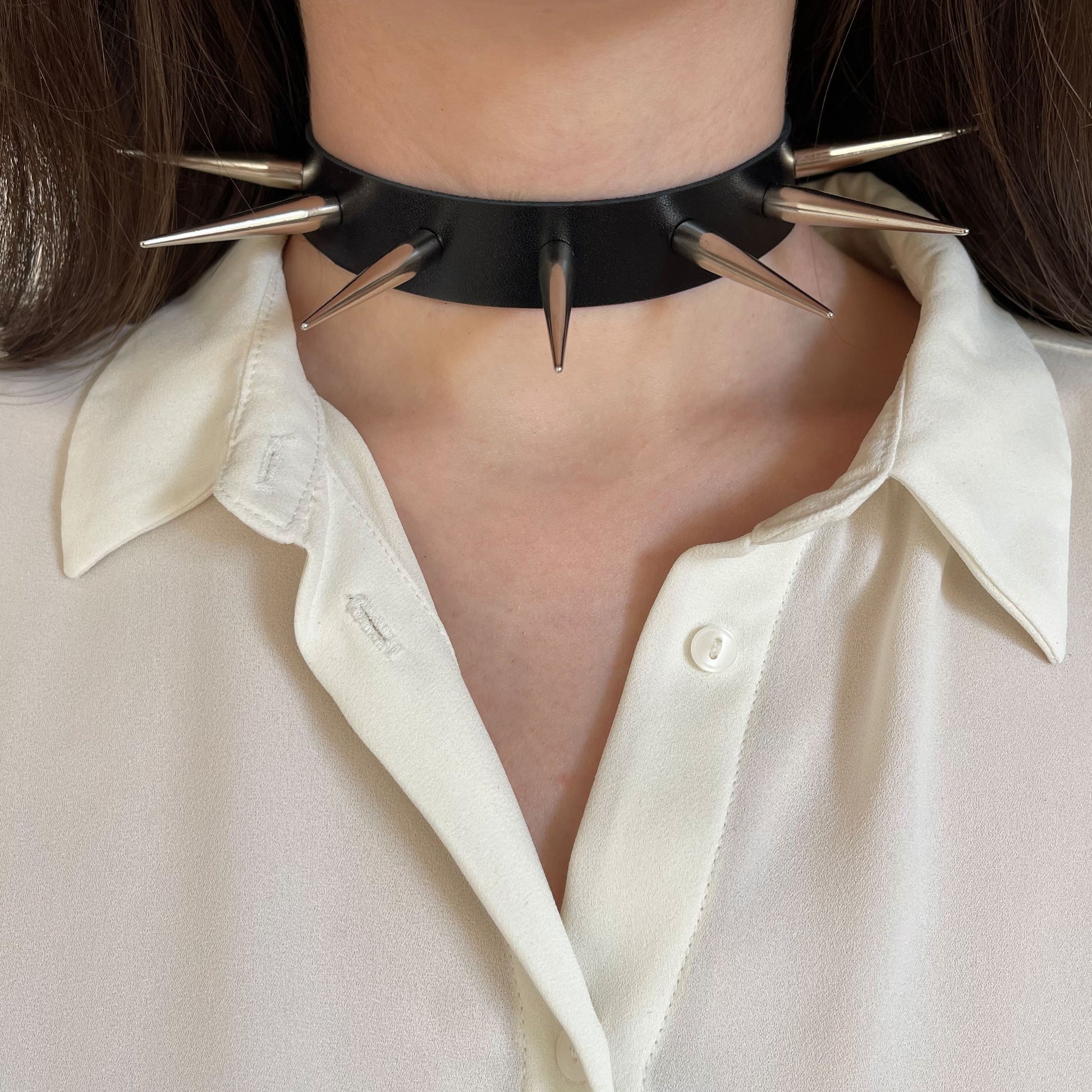 Leather spiked collar worn on the neck, front view, with long silver-colored cone spikes
