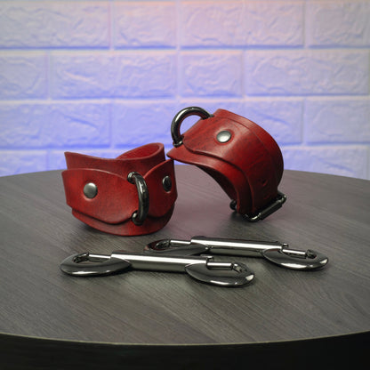 Pair of red leather cuffs with metal hooks on a dark surface.